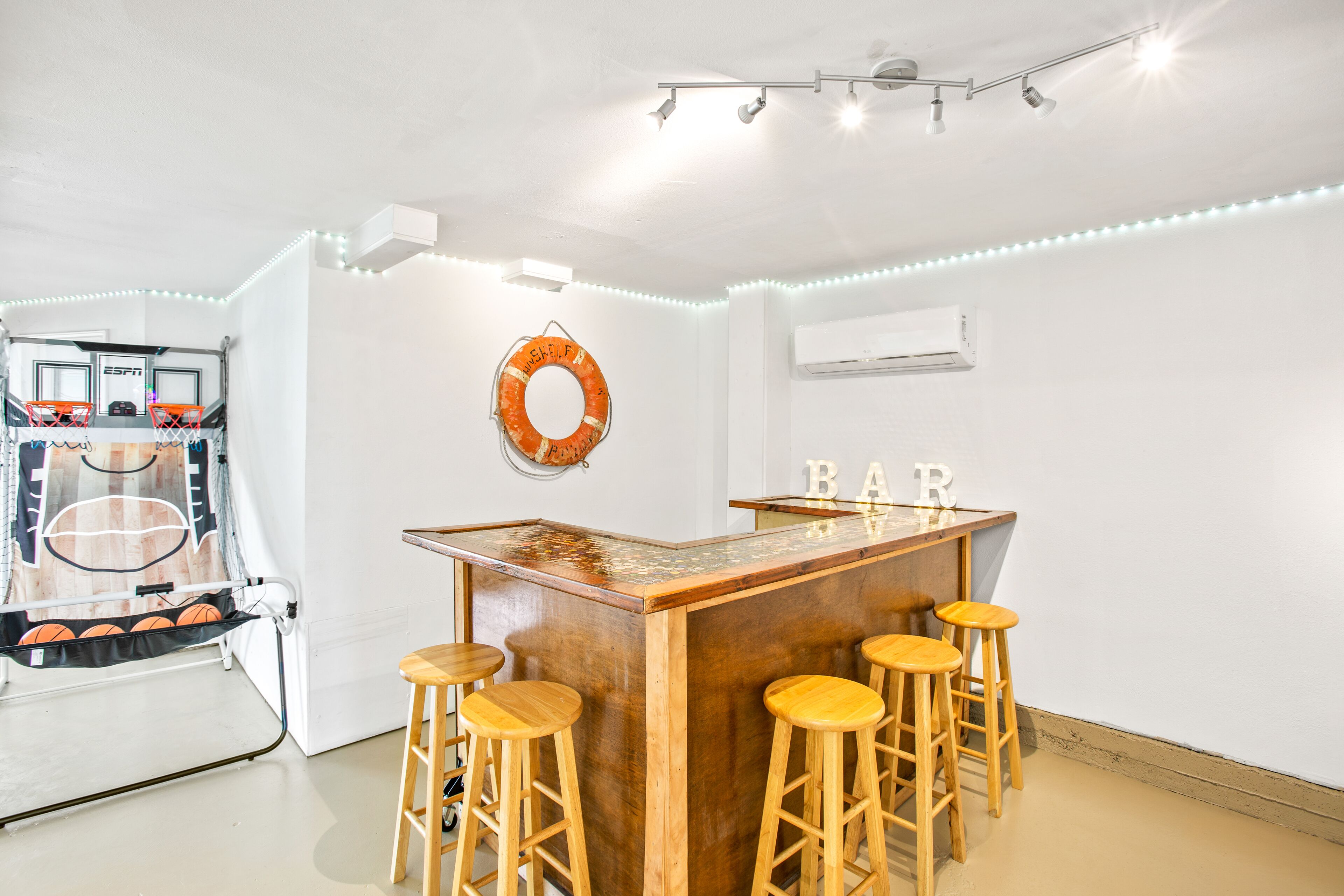 Zona de bar con taburetes de madera, un aro de baloncesto y un flotador en la pared.
