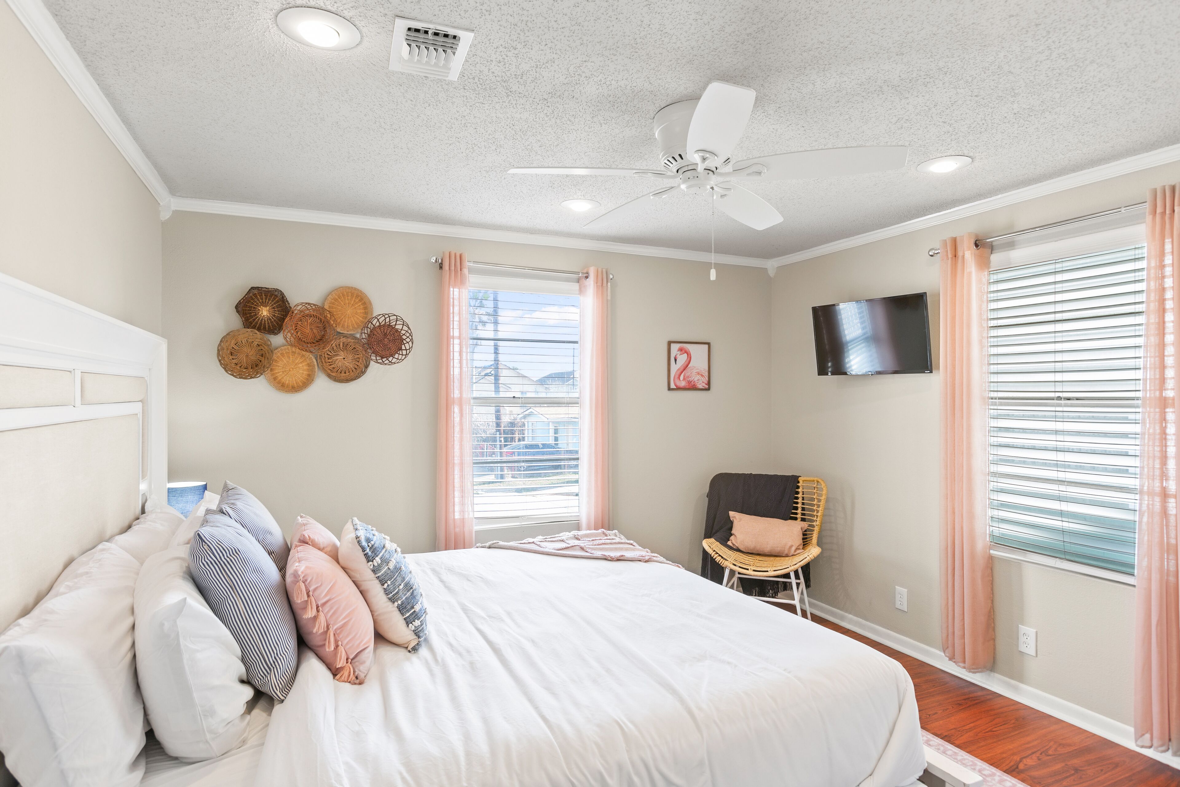 Un dormitorio con una cama, ventilador de techo, televisor montado y ventana con persianas.