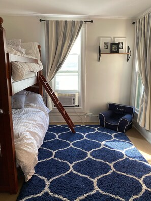 A bunk bed room with a blue patterned rug, a ladder, a small chair, and a window with curtains. - Historic Victorian on the Park (Little Falls)