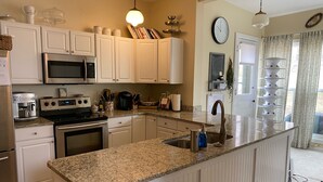 A kitchen with white cabinets, a granite countertop, stainless steel appliances, and a hanging light fixture. - Historic Victorian on the Park (Little Falls)