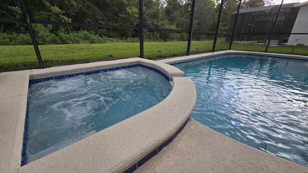 A swimming pool with a hot tub area, surrounded by a fence and greenery. - Big house with private pool near to Dinsey and other theme parks (Kissimmee)