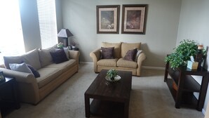 A living room with two beige sofas, a dark wooden coffee table, and a small side table with a plant. - Big house with private pool near to Dinsey and other theme parks (Kissimmee)