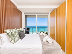 A hotel room with a bed, a small seating area, a view of the ocean, and a balcony with a grill.