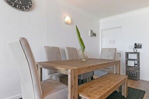 Ein Essbereich mit einem Holztisch und Stühlen, einer Vase mit einer Pflanze, einer Wanduhr und einem kleinen Regal mit einem Radio.