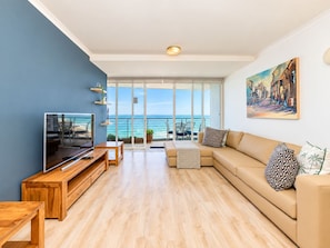 A modern living room with a large TV, wooden furniture, a sofa with patterned cushions, and a painting on the wall.