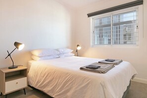 Een slaapkamer met een bed, twee bedlampen, een raam en een nachtkastje met een lade.