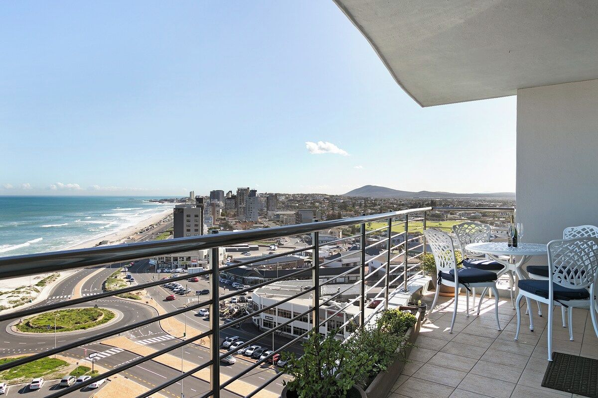 Un balcón con vistas a la playa y al paisaje urbano, incluyendo una glorieta y edificios.