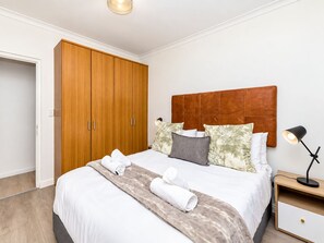 A bedroom with a bed, a wardrobe, a nightstand, and a lamp. - Chic Beachfront Apt with Table Mountain views (Cape Town)
