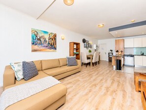 A modern living room with a sofa, a dining table, and a kitchen area with cabinets and a dishwasher. - Chic Beachfront Apt with Table Mountain views (Cape Town)