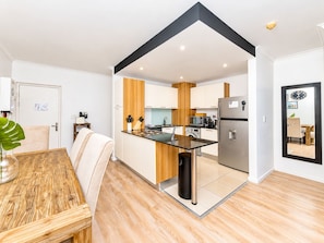 A modern kitchen with a central island, a dining area with a wooden table, and a living space with a sofa.