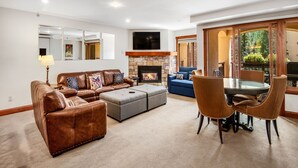A living room with a brown leather sofa, a glass-top dining table with chairs, a fireplace, and a large mirror on the wall. - Ski In and Out Condo in Lionshead Village w/ Pool, Hot Tubs, and Lovely Views (Vail)