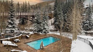 A pool area with a wooden deck, lounge chairs, and a small pool. - Ski In and Out Condo in Lionshead Village w/ Pool, Hot Tubs, and Lovely Views (Vail)