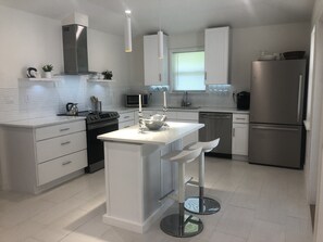 A modern kitchen with white cabinetry, stainless steel appliances, and a central island with stools.