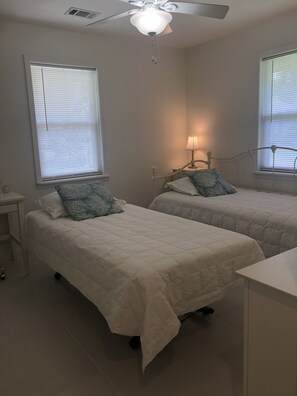 A bedroom with two beds, a ceiling fan, and a bedside table with a lamp.