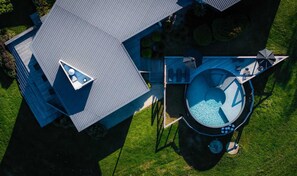 Vue aérienne d’une maison moderne dotée d’un toit triangulaire au design original, d’un grand bassin circulaire et d’une pelouse bien entretenue.