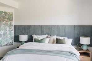 A neatly made bed with a grey headboard, two bedside tables with lamps, and a floral artwork on the wall.