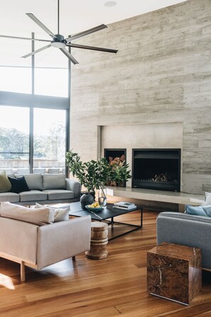 A modern living room with a fireplace, a ceiling fan, and large windows.