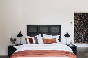 A bed with a black headboard, white bedding, and brown accents, flanked by black nightstands with lamps and a small plant.