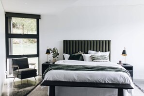 A modern bedroom with a large bed, a chair, a nightstand, and a window.