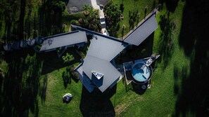 An aerial view of a house with a sloped roof, a swimming pool, and a well-maintained lawn.