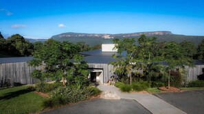 A modern building with a metal roof, surrounded by lush greenery and a clear view of distant mountains.