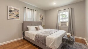 A bedroom with a bed, a window with curtains, and artwork on the wall.