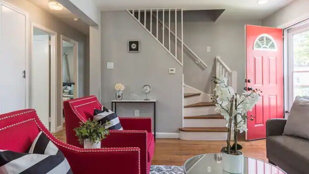 A living room with a staircase, red and grey sofas, a coffee table, and a red door.