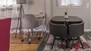 A modern office space with a round table, a grey office chair, a red chair, a floor lamp, and a window with sheer curtains.