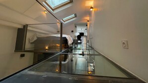 A narrow hallway with a glass floor leading to a bedroom with a bed and a skylight. - Bastille Sedaine (Paris)