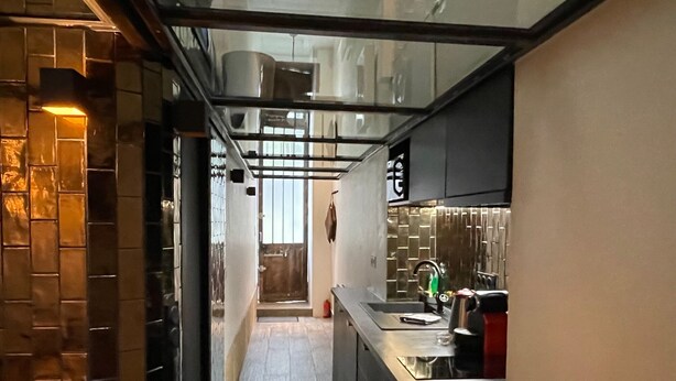 A narrow hallway with a kitchen area on the right, featuring a sink, stove, and cabinets. - Bastille Sedaine (Paris)