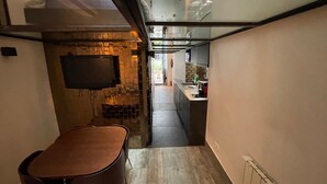 A modern kitchen with a flat-screen TV mounted on the wall, a dining area with a bench, and a staircase leading to an upper level. - Bastille Sedaine (Paris)