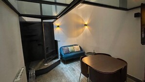 A modern interior with a staircase leading to a loft area, a blue sofa, and a small round table. - Bastille Sedaine (Paris)