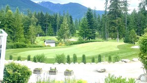 Un campo de golf con un club de campo, rodeado de un bosque denso y montañas.