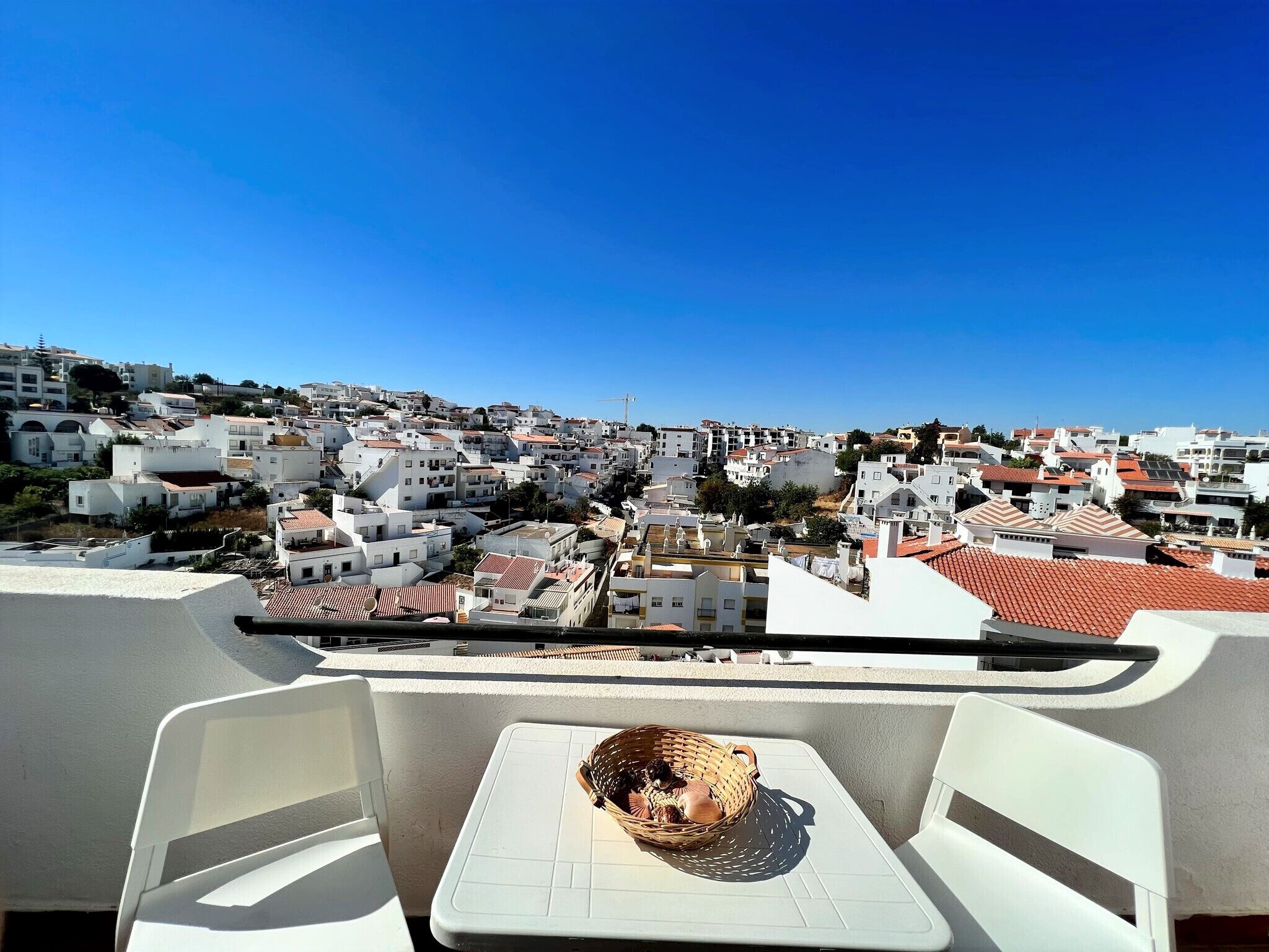 Ein Balkon mit Blick auf eine dicht bebauete Stadt mit weißen Gebäuden und roten Ziegeldächern.
