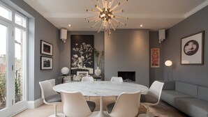 Uma sala de jantar moderna com uma mesa redonda de mármore, cadeiras brancas e um lustre contemporâneo.