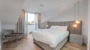 Quarto moderno com uma cama grande, mesas de cabeceira, um banco e vista para a cidade.