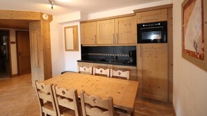 A compact kitchen with wooden cabinets, a black stove, and a dining table with chairs.