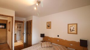 A bedroom with a wooden headboard, two bedside tables with lamps, a bed with floral-patterned bedding, a wooden door, and a shower area.