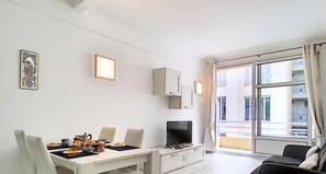 Un salon moderne comprenant un coin repas, un téléviseur et une grande fenêtre offrant une vue sur la ville.
