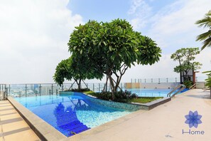 Ein Pool auf dem Dach mit freiem Blick auf die Stadtlandschaft, umgeben von üppiger Bepflanzung und einer Glasbarriere.
