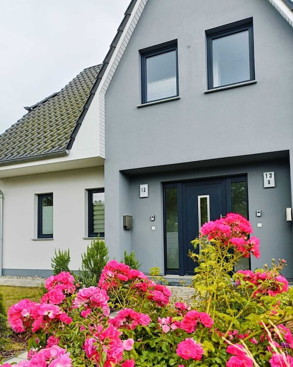 A two-story house with a grey facade, two windows on the upper floor, and a dark blue door. - A Family Dream: Cranes, Deer, Lagoons… Nature and Relaxation (Fuhlendorf)