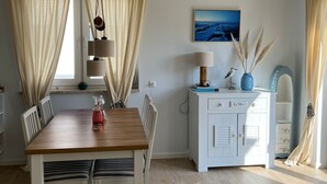 Un comedor con mesa de madera, sillas blancas, un armario blanco con cajones y un cuadro en la pared.