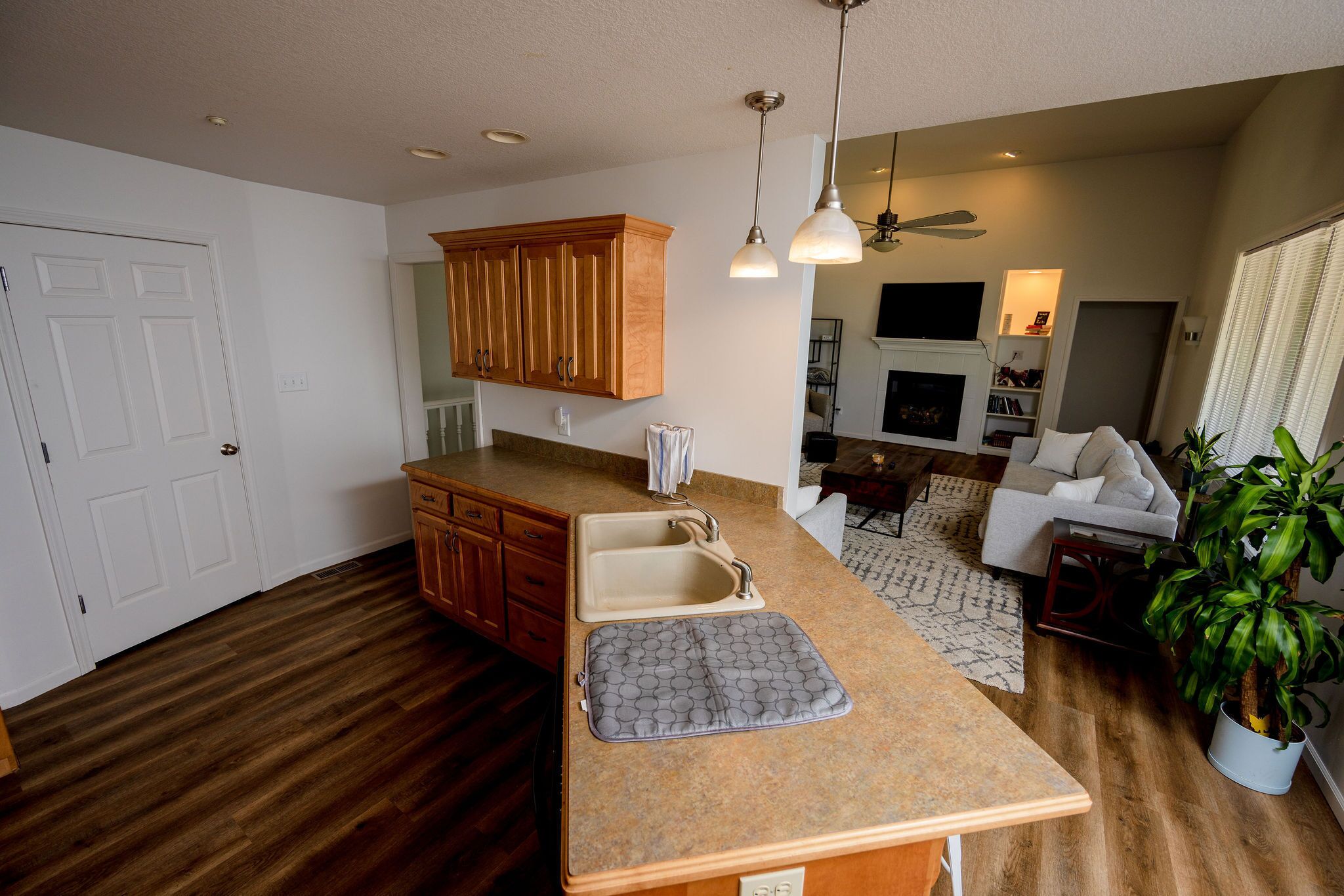 A kitchen with wooden cabinets, a countertop, and a sink. There is a ceiling fan and a plant in the living area.