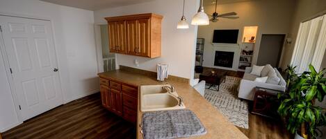 A kitchen with wooden cabinets, a countertop, and a sink. There is a ceiling fan and a plant in the living area.