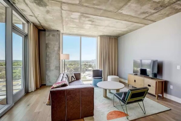 Un salon moderne avec une grande fenêtre, un canapé, une table basse, un téléviseur et un meuble.