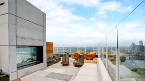 En tagterrasse med moderne siddepladser, et glasgelænder og udsigt over byen.
