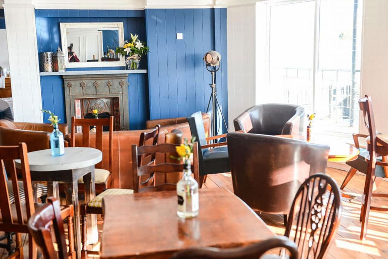 A cozy dining area with wooden tables and chairs, a fireplace, and a large window providing natural light.