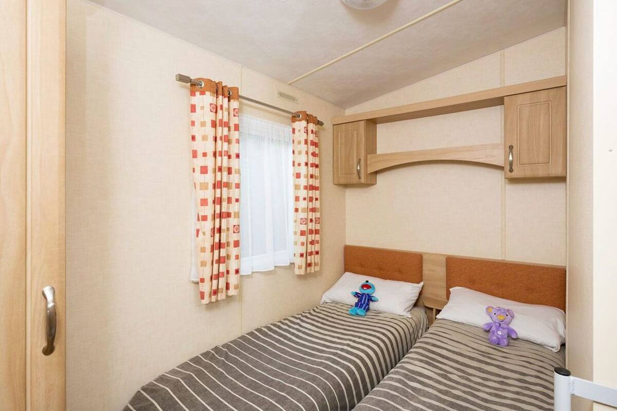Une petite chambre à coucher accueillante, avec deux lits simples, une tête de lit en bois et une armoire intégrée.