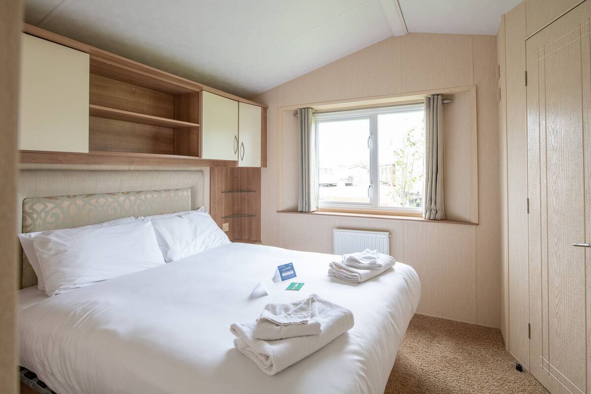Une chambre d’hôtel avec un lit, une fenêtre avec des rideaux, une armoire en bois et une petite étagère au-dessus du lit.