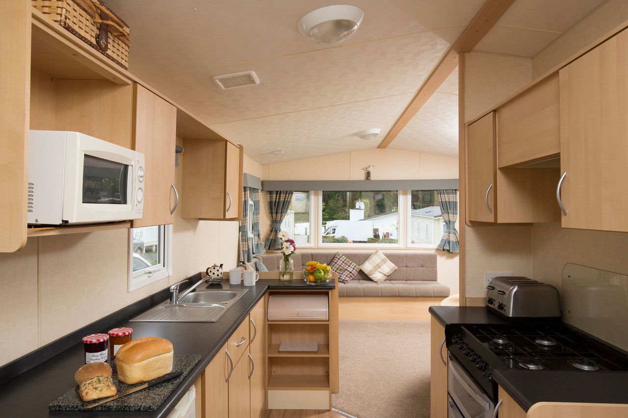 A compact kitchen with a microwave, toaster, and stove. There is a small sink and a window overlooking a garden.